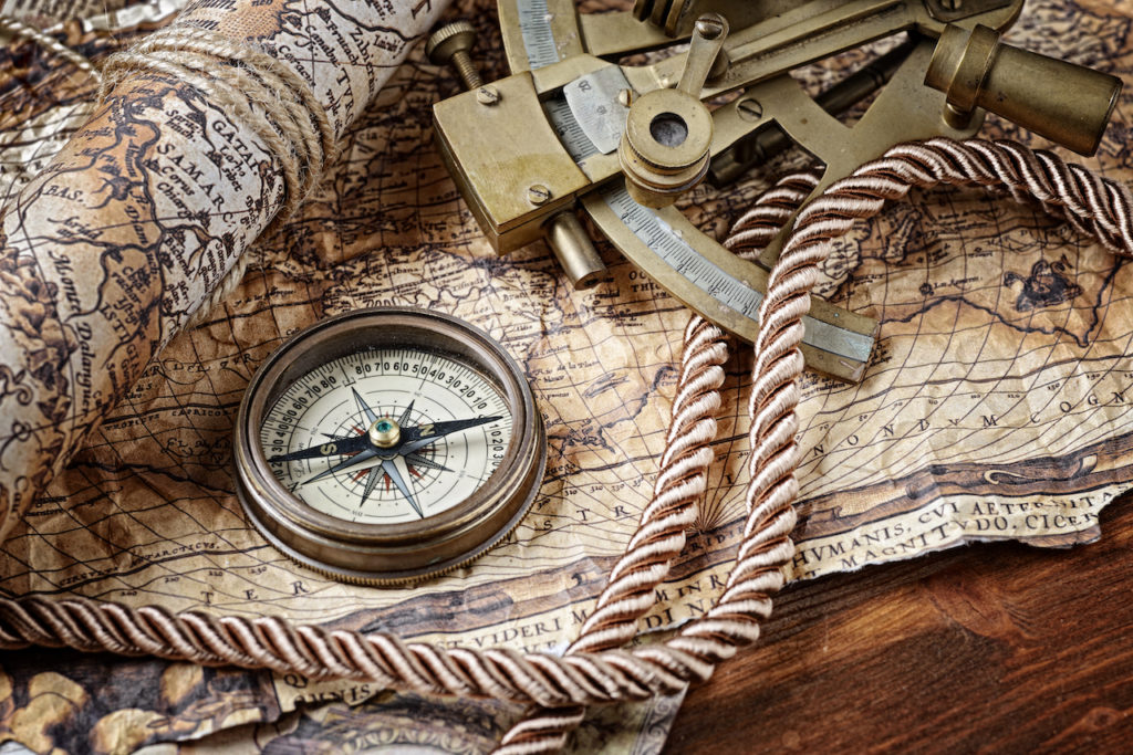 A collection of nautical items rest upon a desk: a sextant, map, rope and compass.