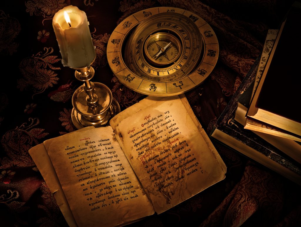 An old open book accompanied by a compass and a candle