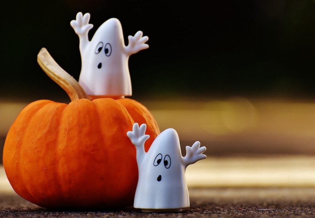 Two porcelain ghosts and a pumpkin, one stands on top of it and one next to it.