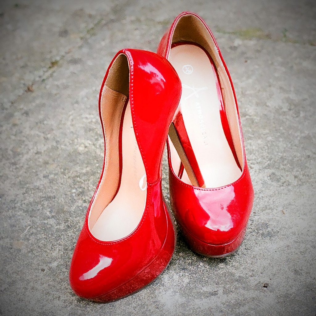 A pair of red high heeled shoes sits upon the floor.