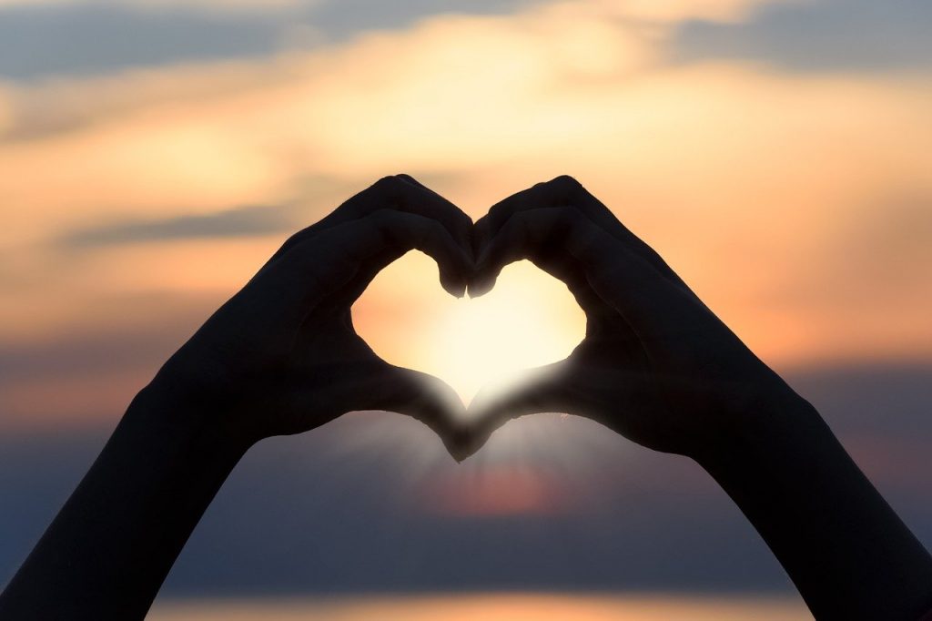 Hands forming a heart in front of a sunset