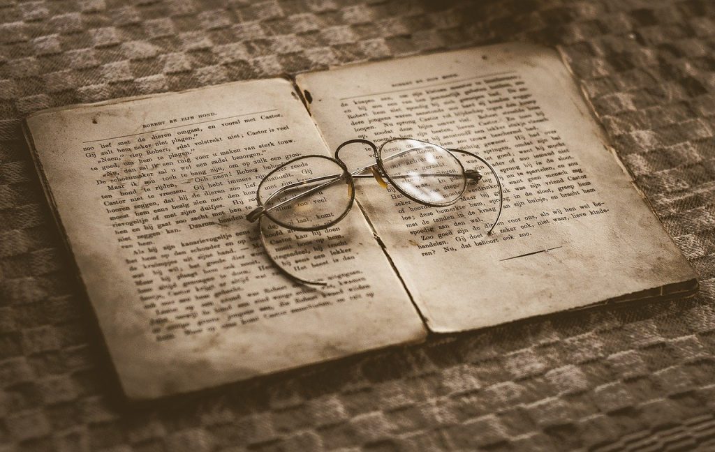 An old book lies splayed on a table, a pair of glasses resting on it.