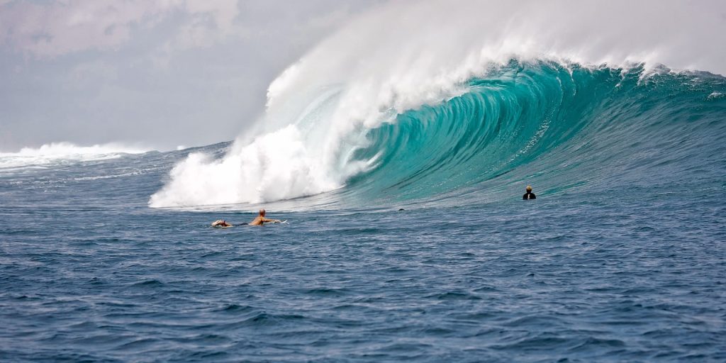 A great wave crashes down, two surfers attempt the wave.