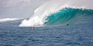 A great wave crashes down, two surfers attempt the wave.