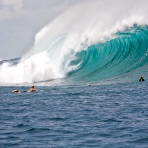 A great wave crashes down, two surfers attempt the wave.