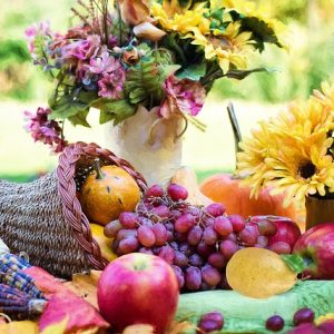 A cornucopia sits upon an outdoor table, surrounded by flowers.