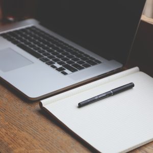 A laptop sits on a desk, an empty notepad lying open next to it.