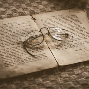 An old book lies splayed on a table, a pair of glasses resting on it.